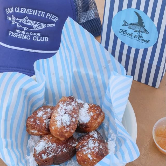 Powdered-sugar beignets with a Hook & Cook fishing-club hat and blue-and-white striped bag.